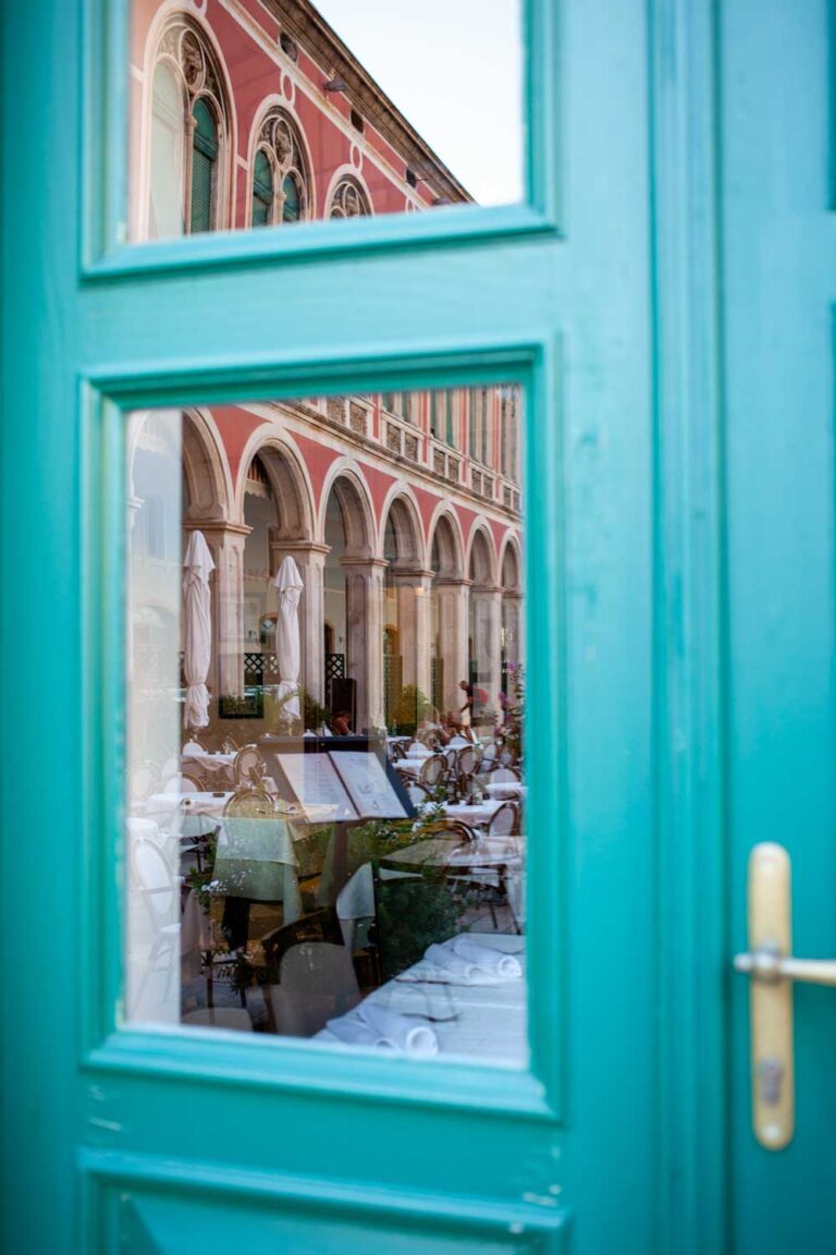a photograph of a blue wooden door and reflection of restaurants in Peristyle central square near the entrance of Diocletian's Palace in Split, Croatia
