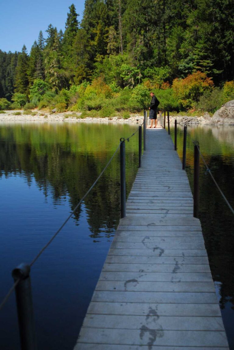 a man is crossing a bridging over lake with reflections in Jedediah Smith Redwoods State Park in Del Norte County, California