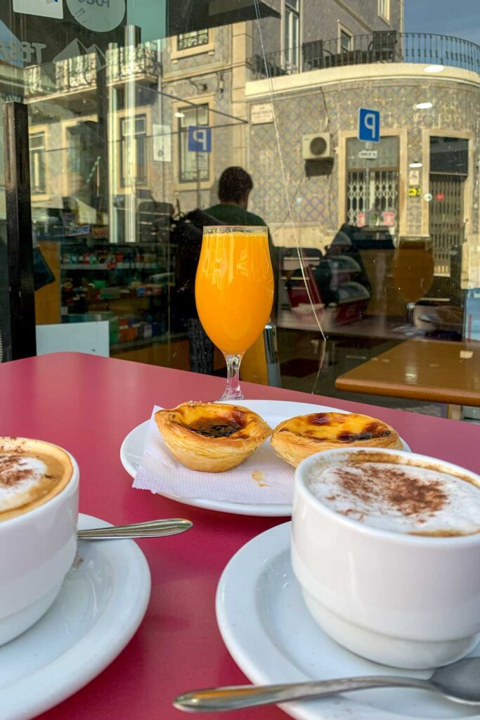 photograph of breakfast spread at an outdoor cafe in Lisbon, Portugal with pasteis de nata, cappuccinos and orange juice